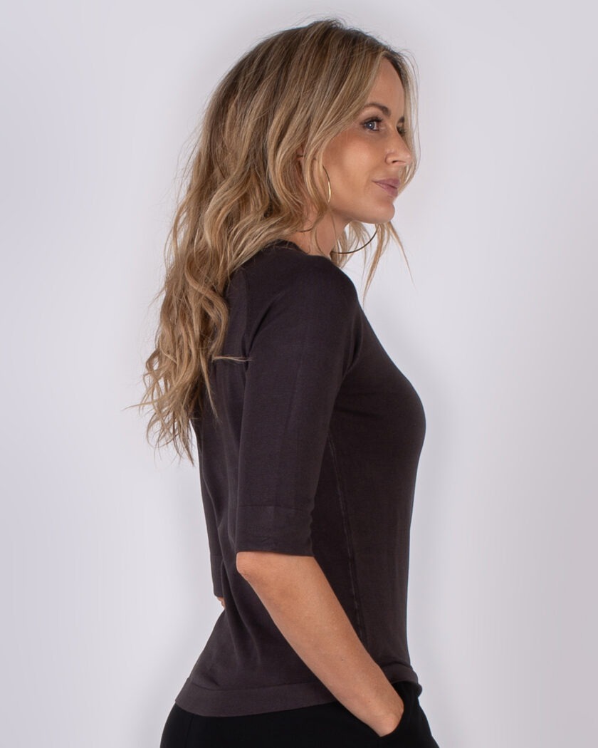 Vrouw in profiel poseert in een donkerbruin, halfmouw shirt uit de Studio AW25-26 collectie.