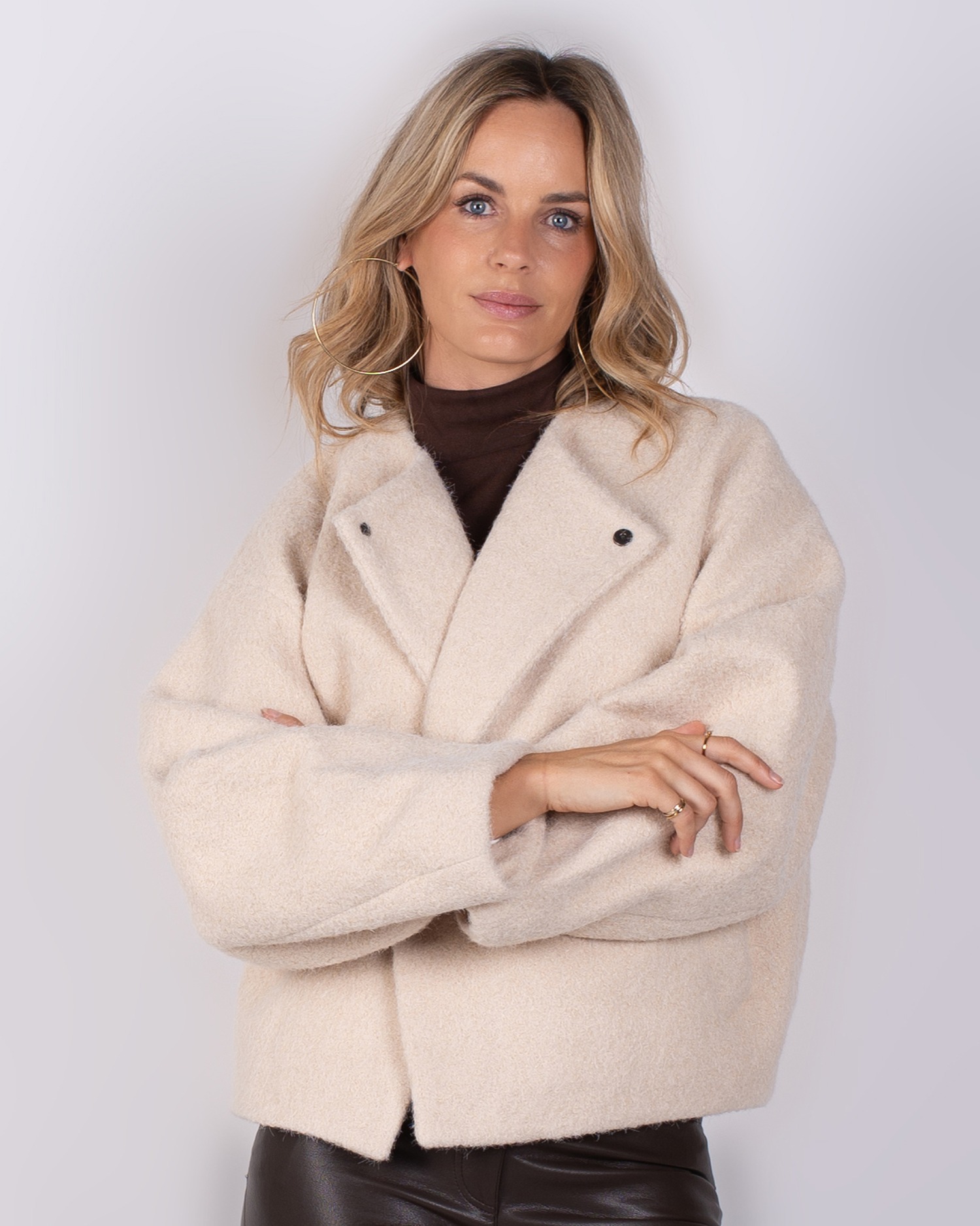 Studio_AW25-26#3-16 Vrouw poseert in een crèmekleurige wollen jas uit de Studio AW25-26 collectie.