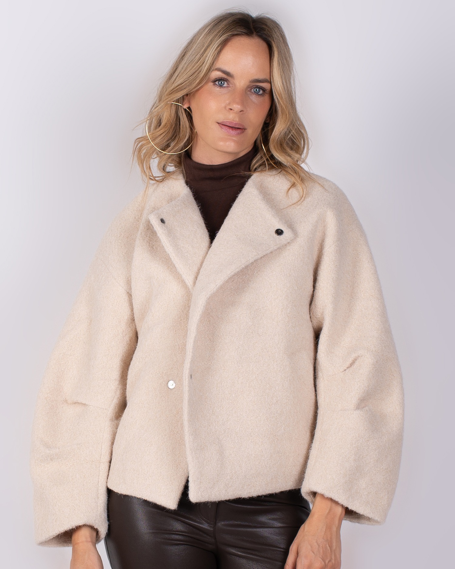 Studio_AW25-26#3-17 Vrouw in een beige, wollen jas uit de Studio AW25-26 collectie, gecombineerd met een bruine coltrui en leren broek.