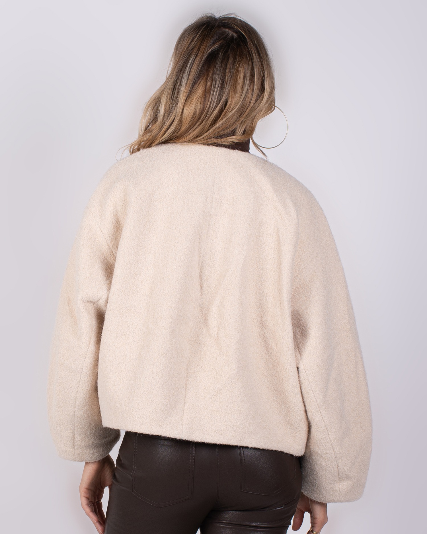 Studio_AW25-26#3-19 Achteraanzicht van een vrouw in een beige fleece-achtige jas en donkerbruine leren broek uit de Studio AW25-26 collectie.
