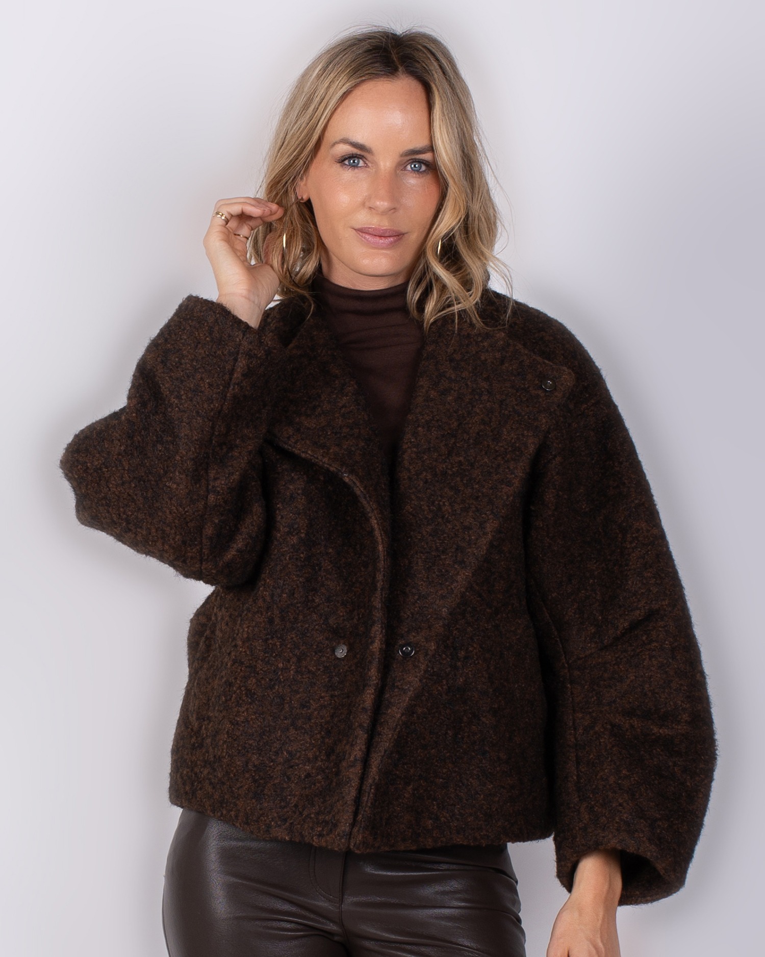 Vrouw draagt een donkerbruine, oversized wollen jas uit de Studio AW25-26 collectie.