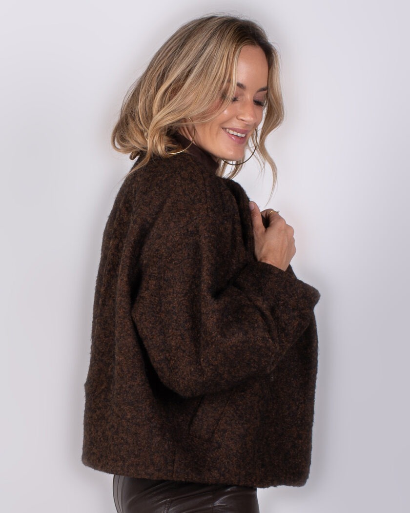 Vrouw poseert in een kort, donkerbruin wollen jasje uit de Studio AW25-26 collectie.
