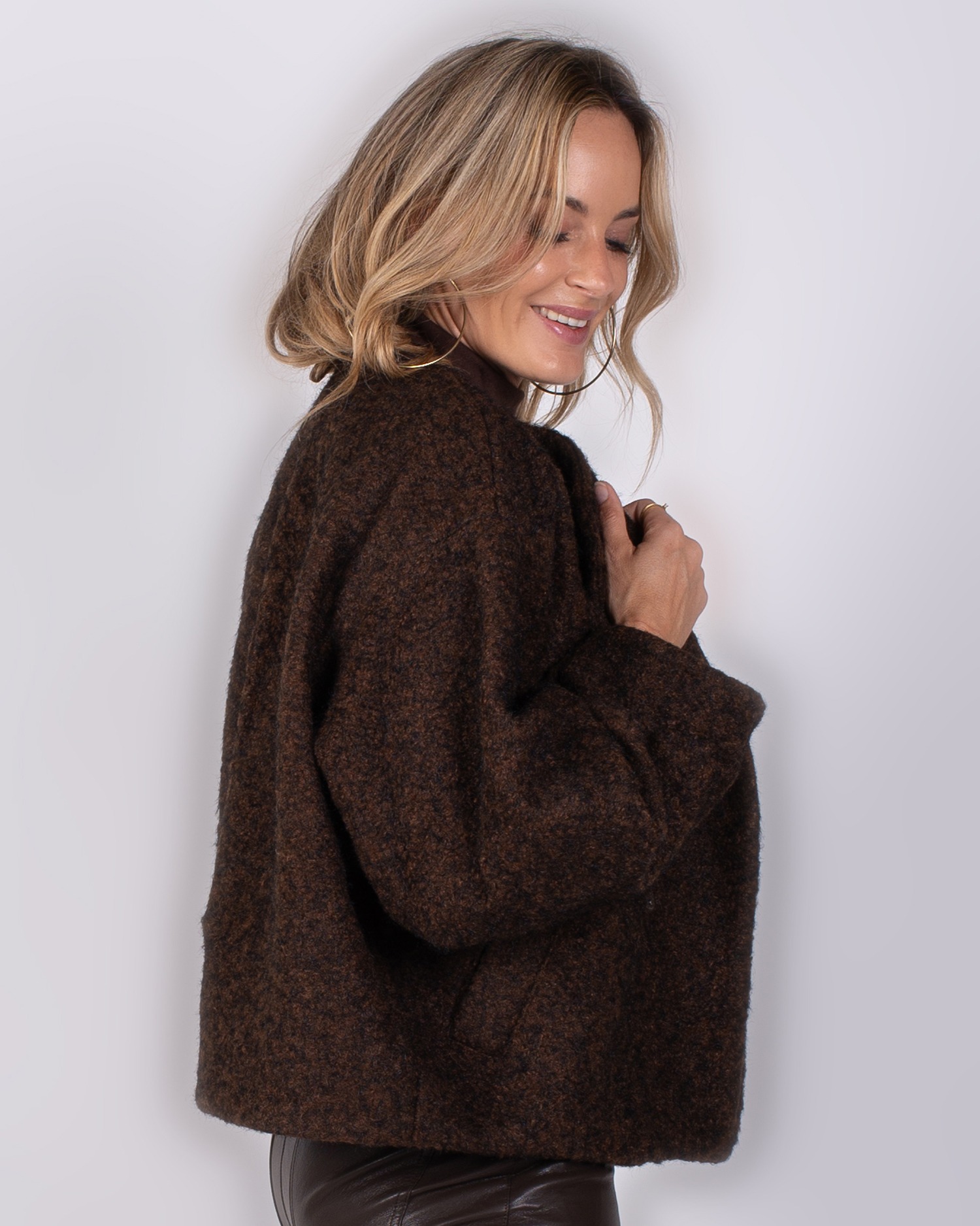 Studio_AW25-26#3-22 Vrouw poseert in een kort, donkerbruin wollen jasje uit de Studio AW25-26 collectie.