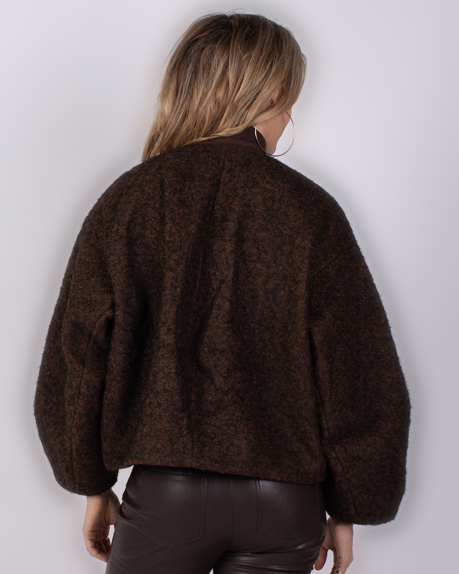 Studio_AW25-26#3-23 Vrouw van achteren in een donkerbruin gemêleerde, wollige oversized jas uit de Studio AW25-26 collectie.