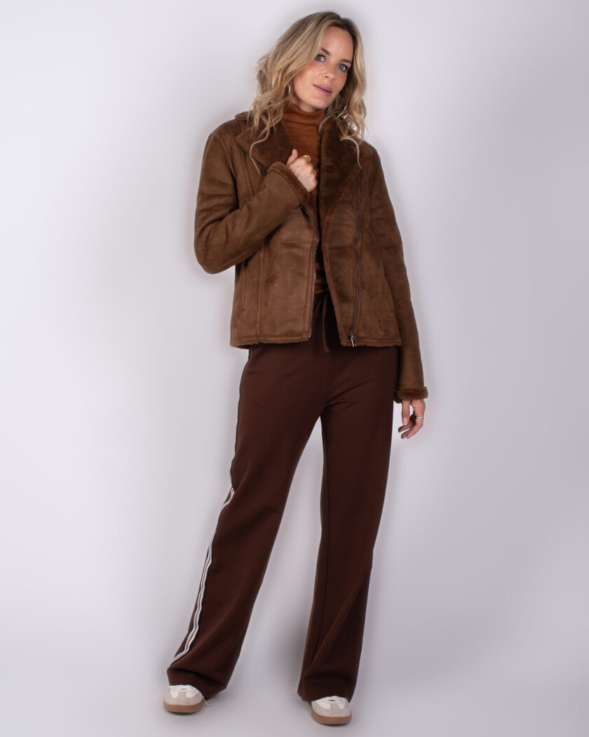 Vrouw draagt een bruine shearling jas met bijpassende broek en sneakers uit de Studio AW25-26 collectie.