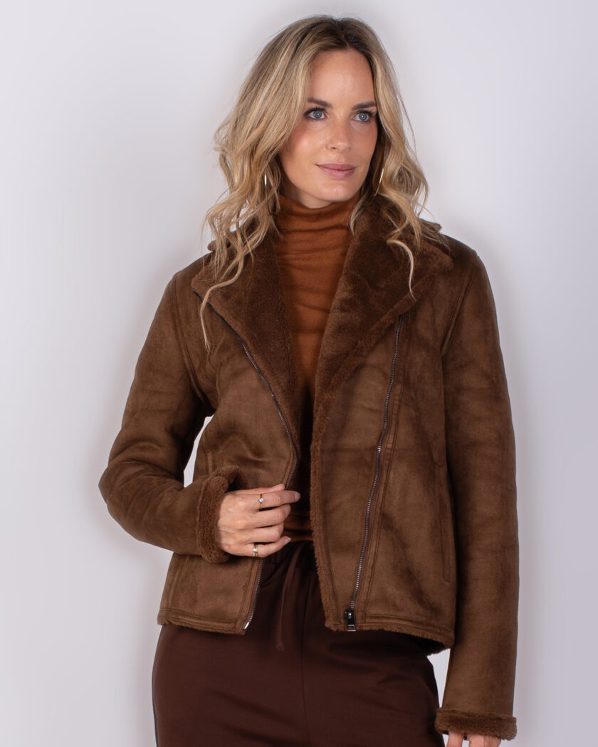 Vrouw draagt een bruine shearling jas met asymmetrische rits uit de Studio AW25-26 collectie.