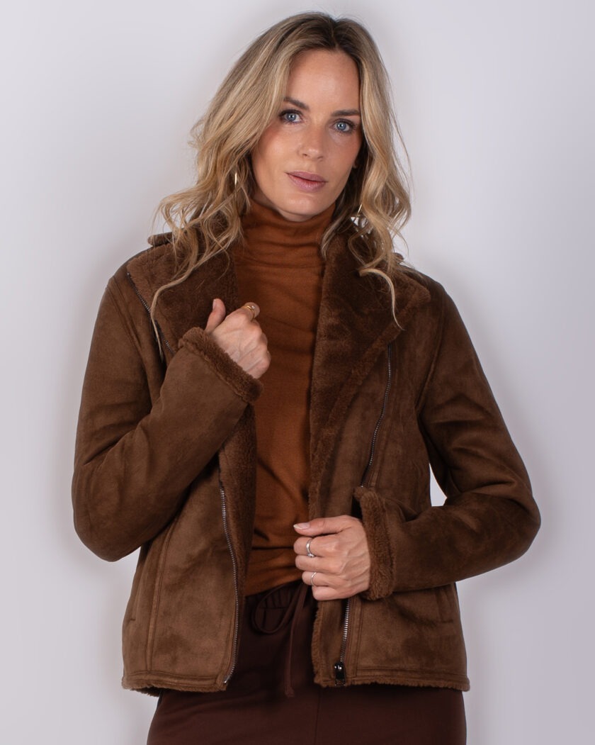 Vrouw draagt een bruine, gevoerde jas en een coltrui uit de Studio AW25-26 collectie.