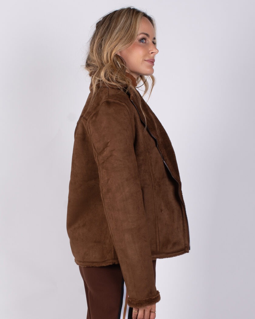 Vrouw in zijaanzicht draagt een bruine suède jas met bontvoering uit de Studio AW25-26 collectie.