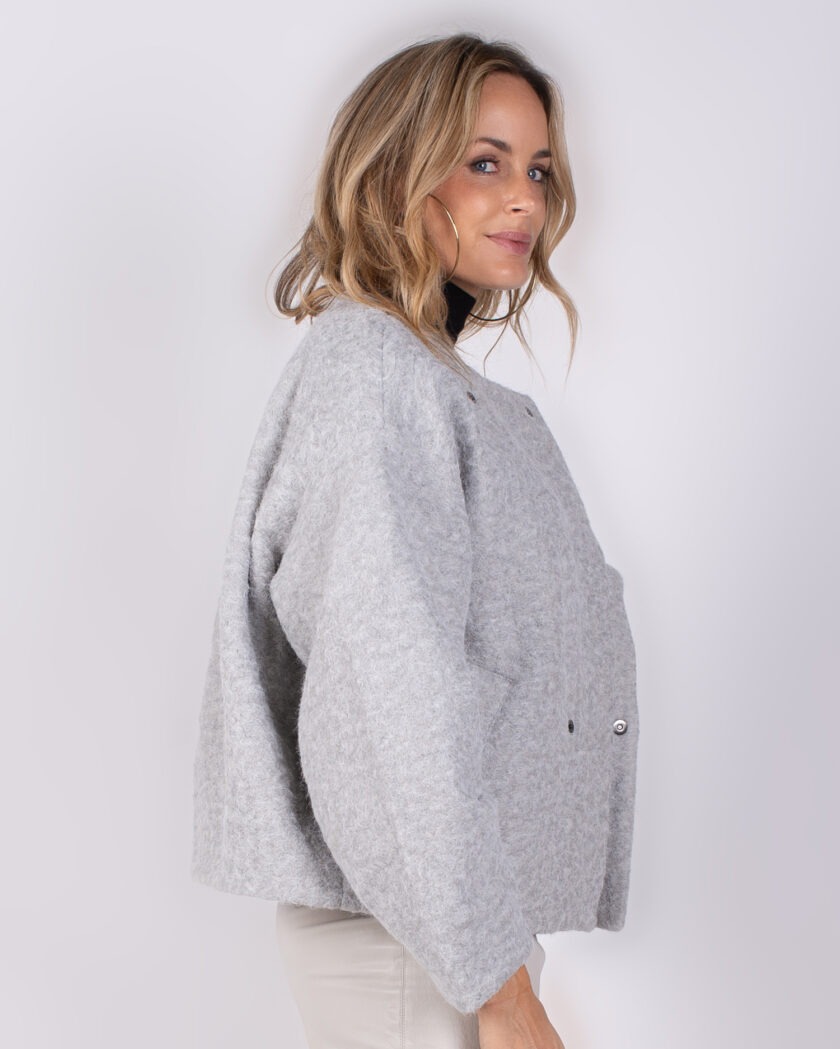 Vrouw poseert in zijaanzicht met een lichtgrijze, wollen jas uit de Studio AW25-26 collectie.