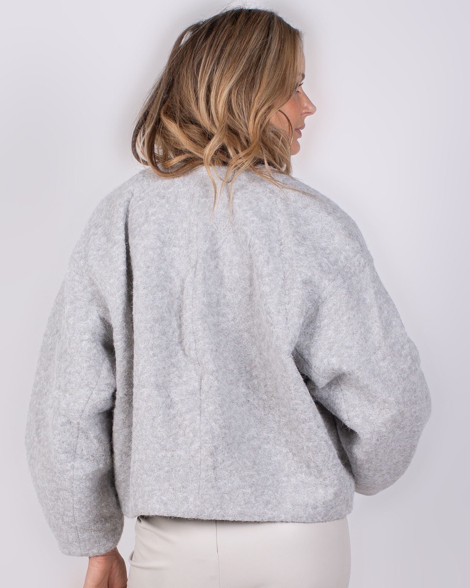 Studio_AW25-26#3-46 Vrouw van achteren in een lichtgrijze, wollige Studio AW25-26 jas.