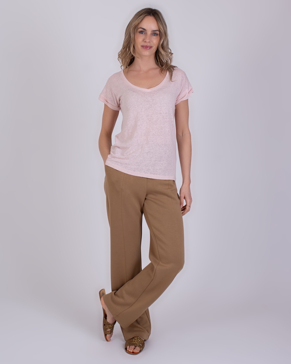 Athene old pink 3 Vrouw draagt een lichtroze Athene T-shirt met V-hals en wijde beige broek.