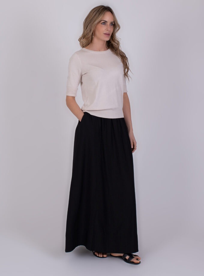 Vrouw draagt de Darwin kit 1, bestaande uit een lichtbeige top en een lange zwarte rok.