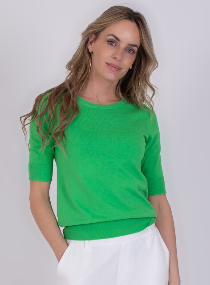 Vrouw draagt een groene Darwin Sea Green trui met halflange mouwen en witte broek.