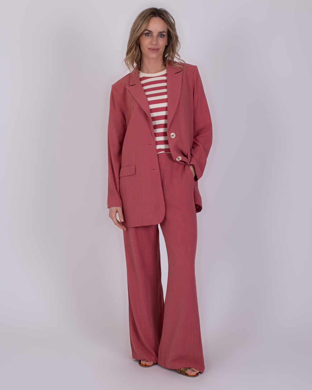 Jodphur raspberry 2 Vrouw draagt een roze Jodphur raspberry broekpak met wijde pijpen en een rood-wit gestreept shirt.