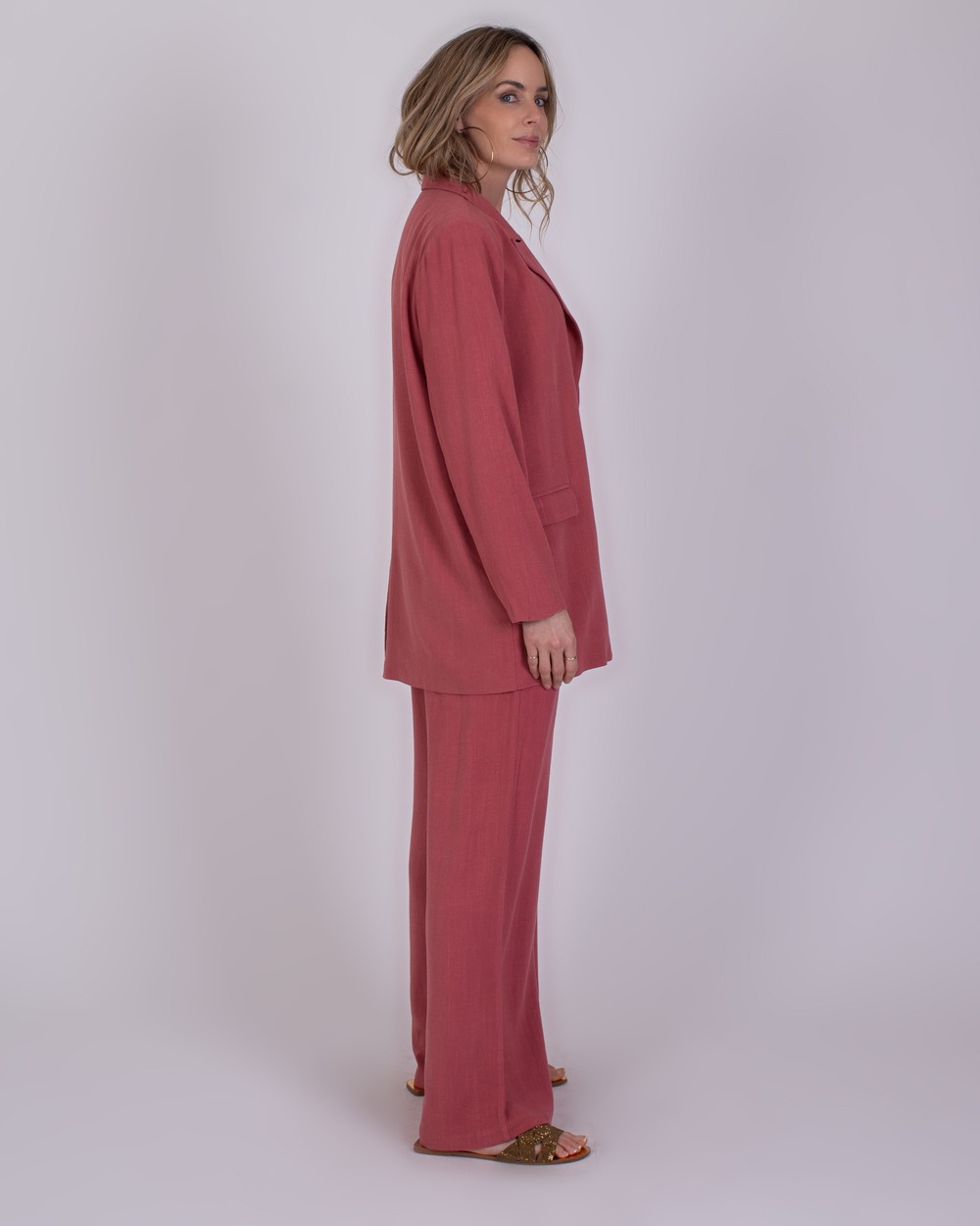 Jodphur raspberry 5 Vrouw met halflang blond haar draagt een losvallend Jodhpur raspberry roze pak met blazer en wijde broek.