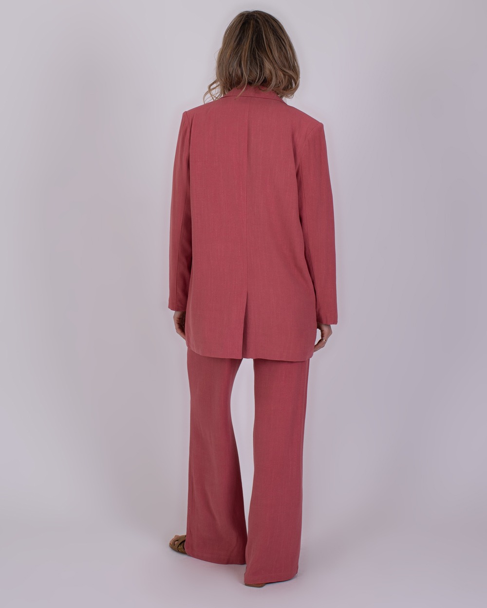 Jodphur raspberry 6 Vrouw van achteren in een framboosroze Jodphur-pak met wijde broek en lange blazer.