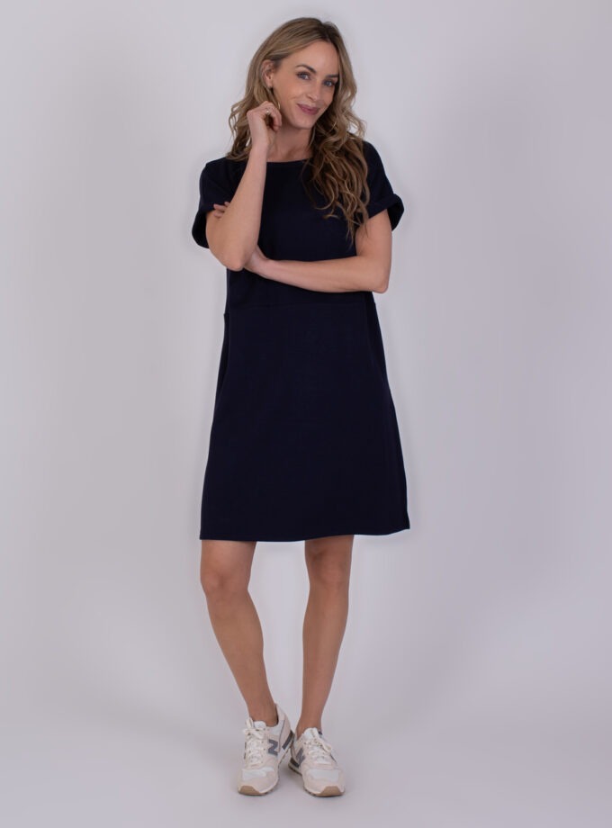 Vrouw draagt een donkerblauwe Liverpool-jurk met korte mouwen en witte sneakers.