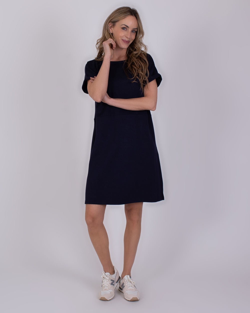 Liverpool navy 4 Vrouw draagt een donkerblauwe Liverpool-jurk met korte mouwen en witte sneakers.