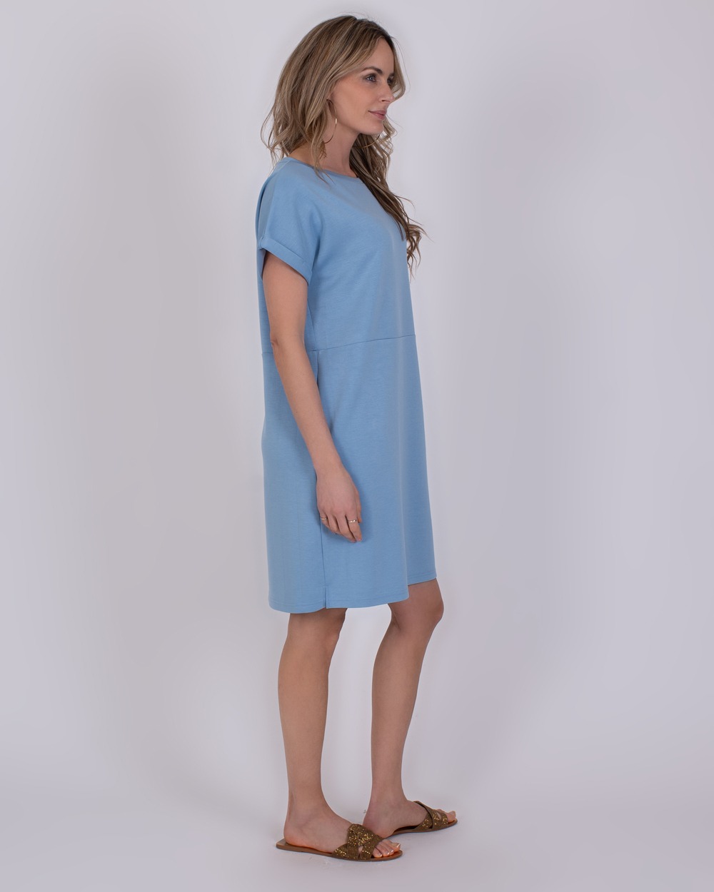 Liverpool soft blue 4 Vrouw in een lichtblauwe "Liverpool soft blue" jurk met korte mouwen en sandalen in zijaanzicht.