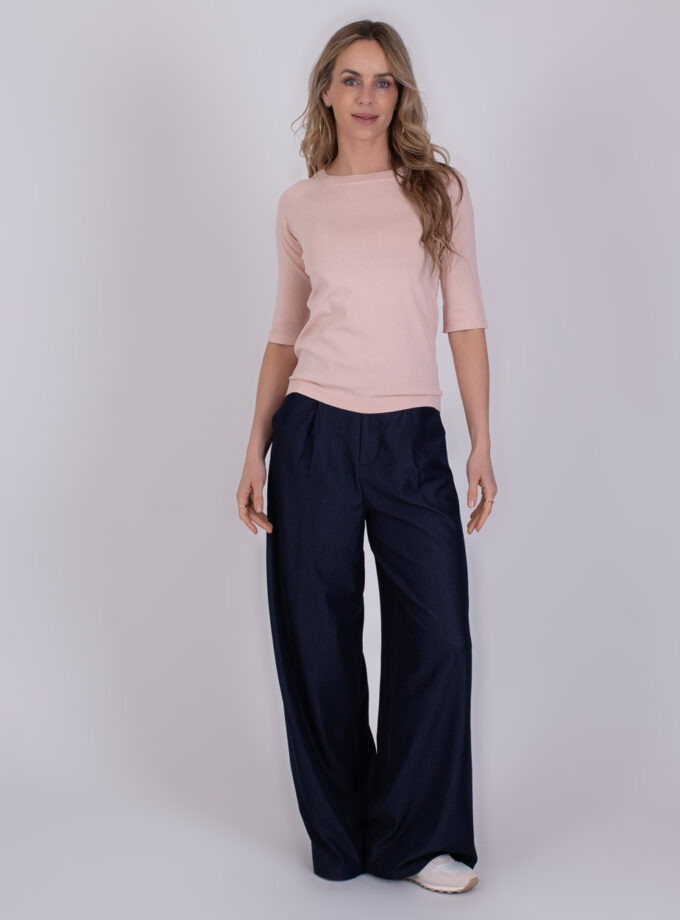 Vrouw draagt een lichtroze Moscow trui met driekwartsmouwen en wijde donkerblauwe broek.