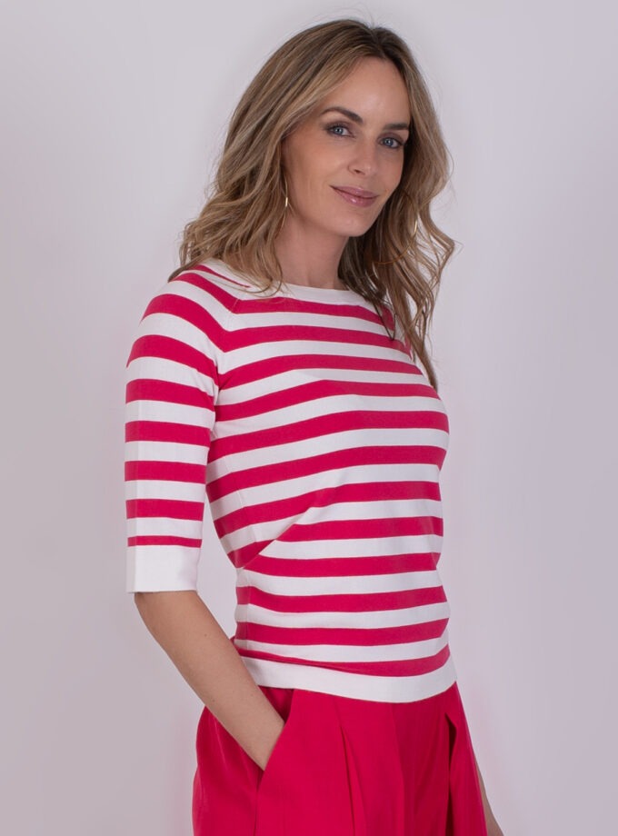 Vrouw met halflang blond haar draagt een Moscow trui met fuchsia-witte strepen en fuchsia broek.