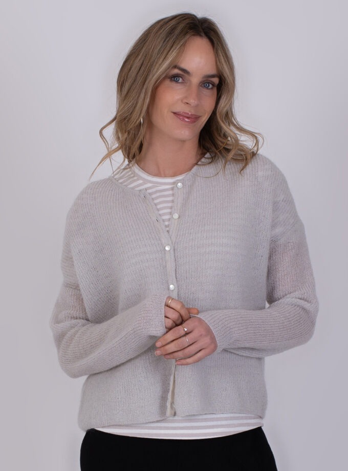 Vrouw draagt een lichtgrijs Narvik-vest met knopen over een gestreept shirt.