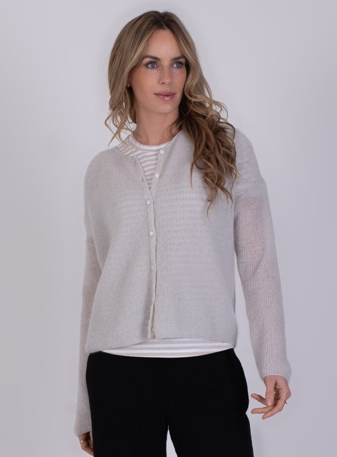 Vrouw draagt een lichtgrijs Narvik-vest met knopen over een gestreept shirt.