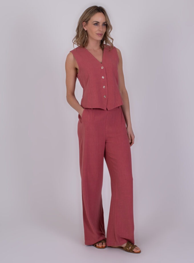 Vrouw draagt een mouwloze, frambooskleurige Surat jumpsuit met wijde pijpen en knoopsluiting aan de voorkant.