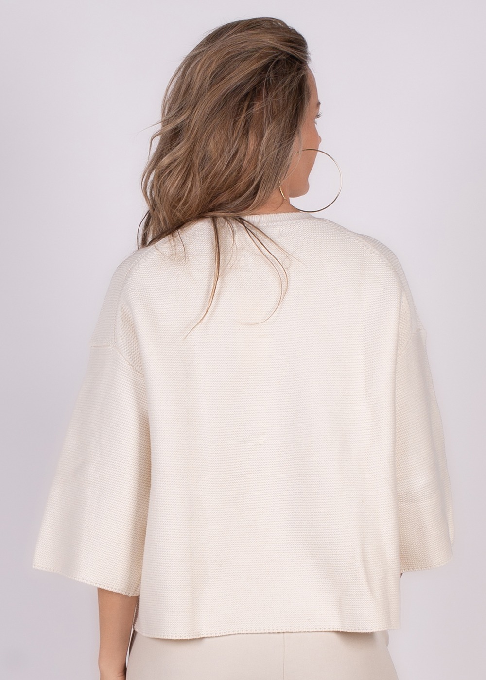 Vrouw van achteren gezien die een offwhite katoenen trui draagt met wijde mouwen.