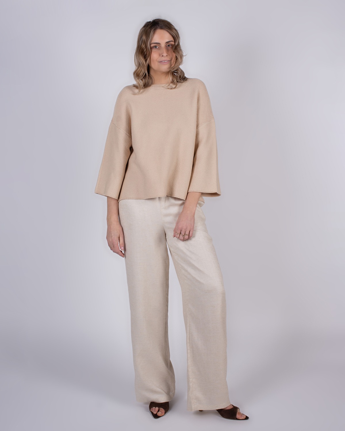 marlien_studio-38 Model draagt een beige trui met wijde mouwen en een lichtgekleurde broek in een studio-omgeving.