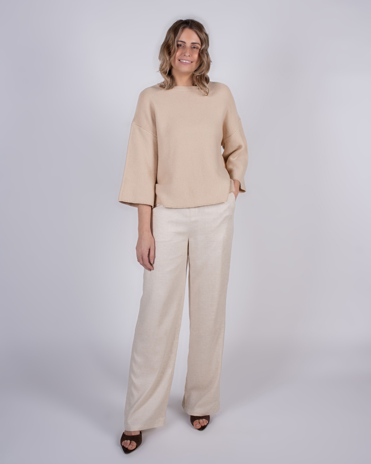 marlien_studio-39 Vrouw poseert in een beige trui en wijde, lichte broek voor een neutrale achtergrond.