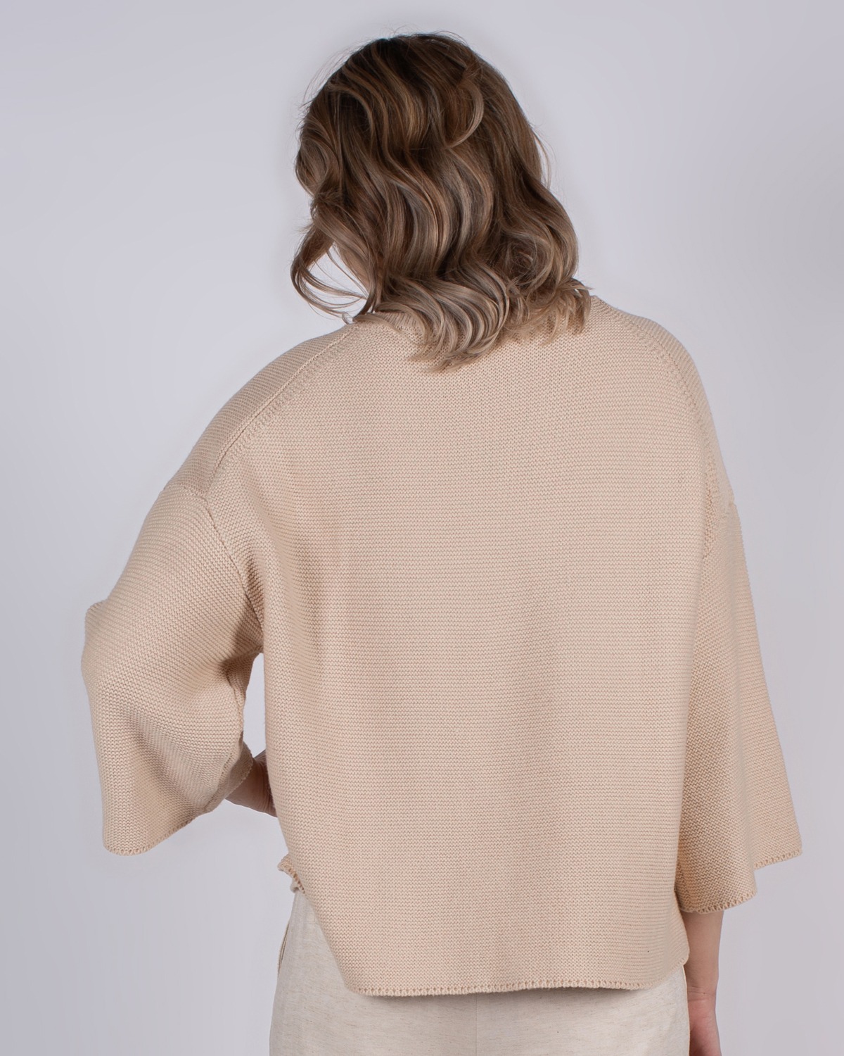 marlien_studio-42 Een vrouw met halflang golvend haar draagt een beige trui met wijde mouwen, gefotografeerd van achteren.