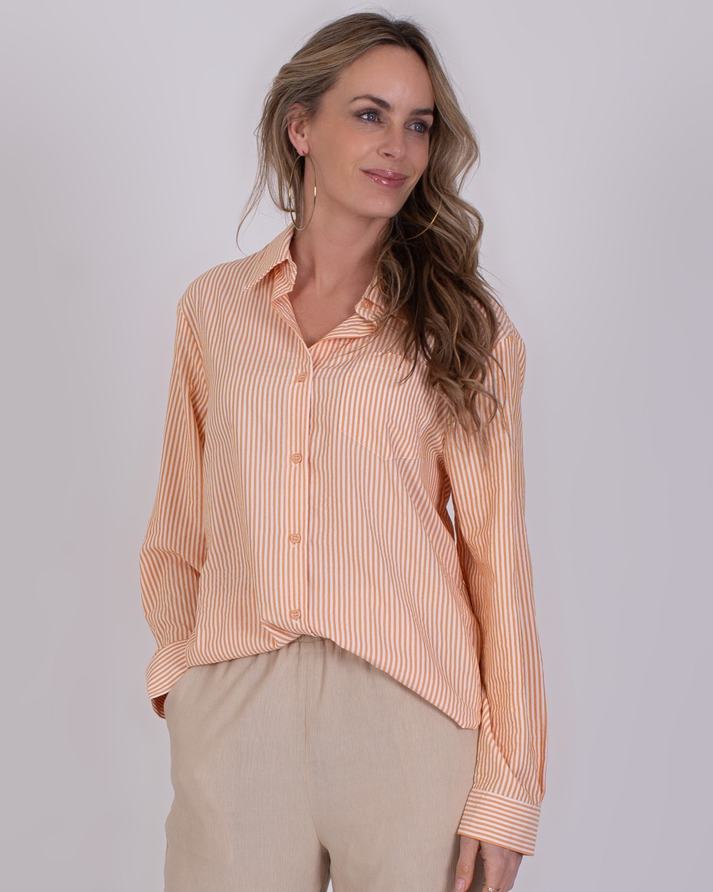 Vrouw draagt een oranje-wit gestreepte blouse genaamd Almeria orange en beige broek.