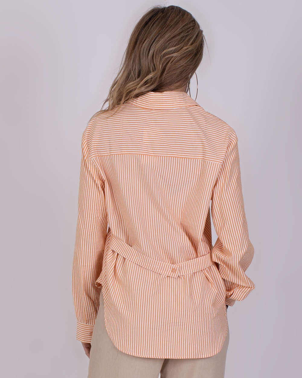 Almeria orange 5 Achteraanzicht van een vrouw met een oranje-wit gestreepte Almeria Orange blouse en beige broek.