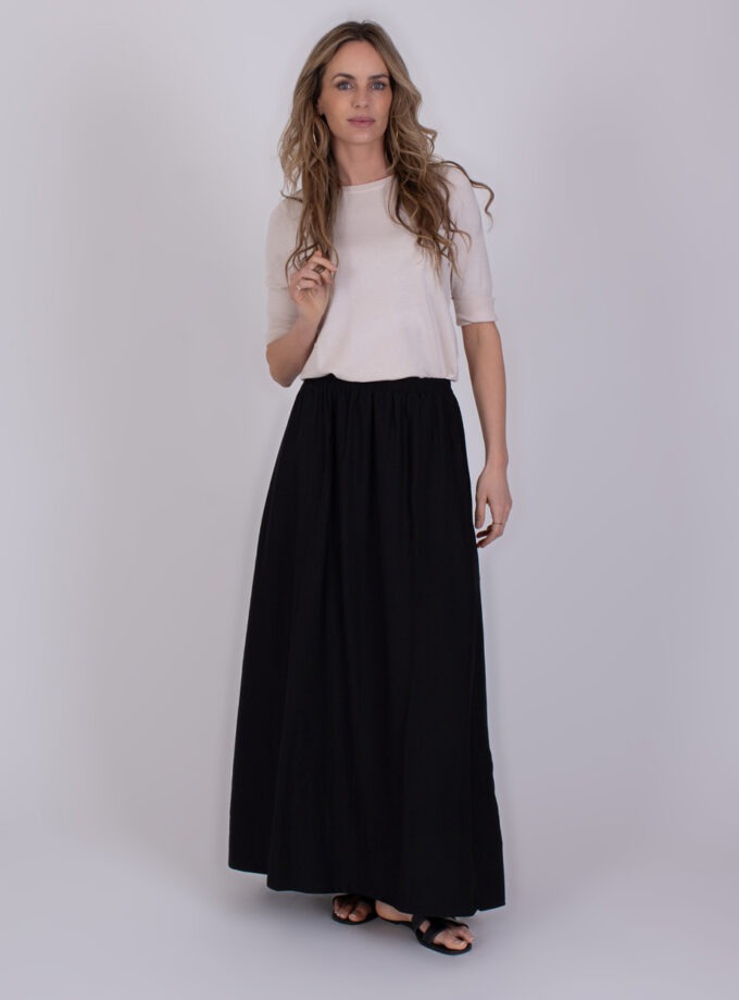 Vrouw draagt een lichtgekleurde top en een zwarte Altos maxi-rok met sandalen.