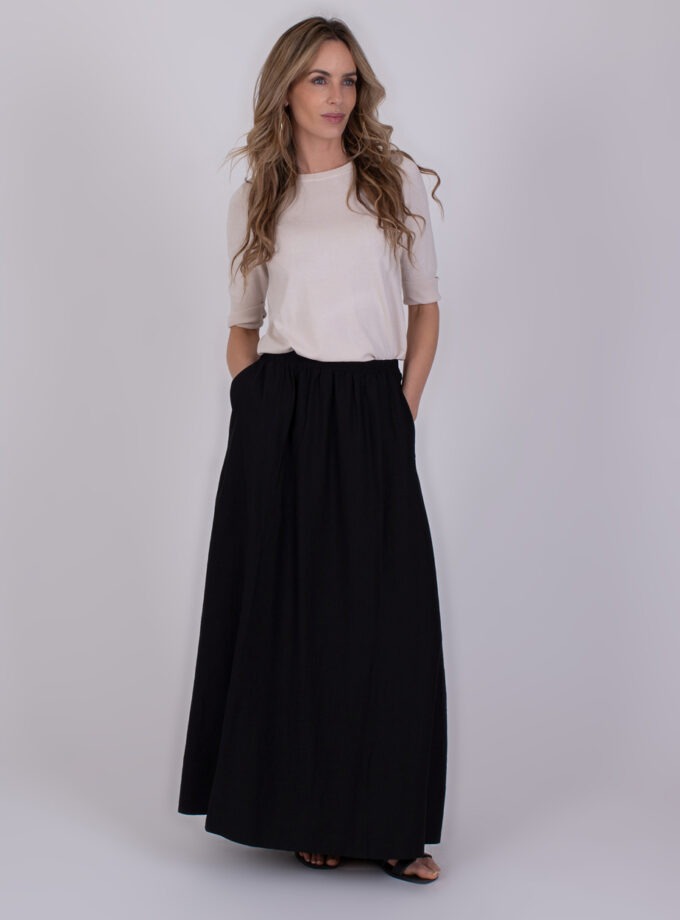Vrouw draagt een beige top en een zwarte Altos Black 5 maxirok met handen in de zakken.