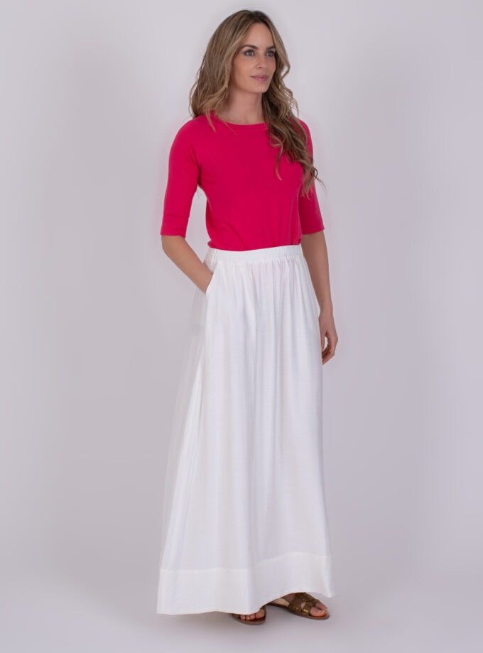 Vrouw draagt een felroze top en een lange off-white Altos rok met sandalen.