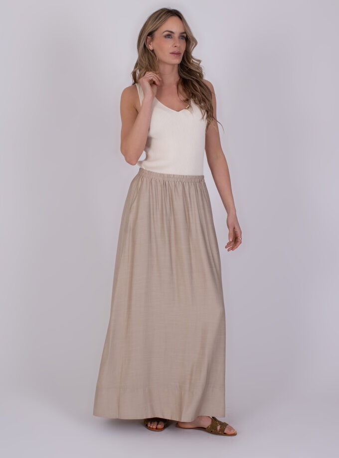 Vrouw draagt een beige Altos Pale maxi-rok met een witte mouwloze top en sandalen.