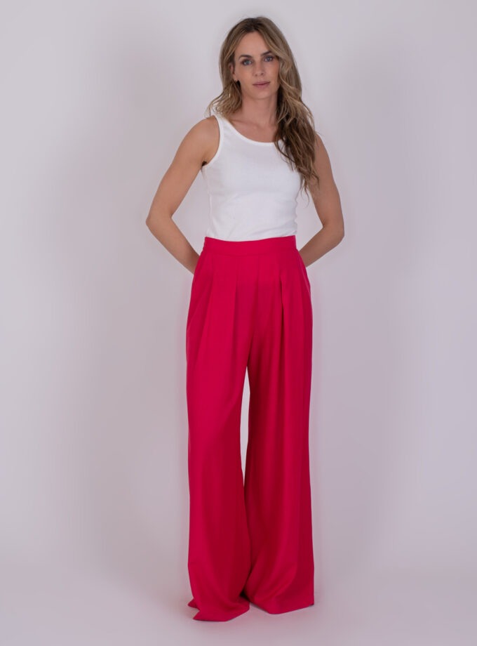 Vrouw draagt een witte tanktop en wijde fuchsiaroze Amfissa-broek tegen een neutrale achtergrond.