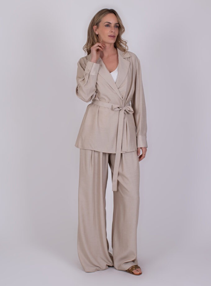 Vrouw draagt een beige Basra Pale 1 broekpak met wijde pijpen en ceintuur in de taille.