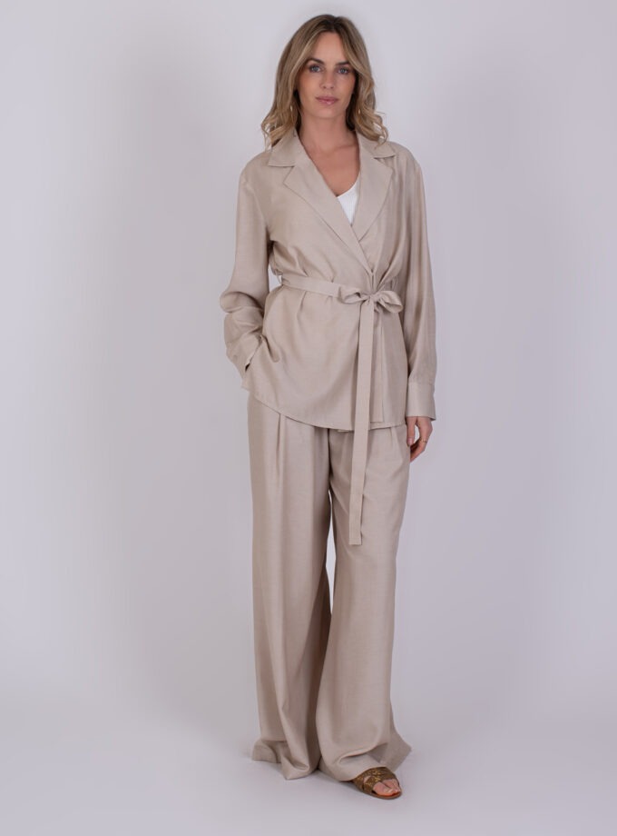 Vrouw draagt een beige Basra Pale 2 broekpak met strikceintuur voor een elegante, ontspannen look.