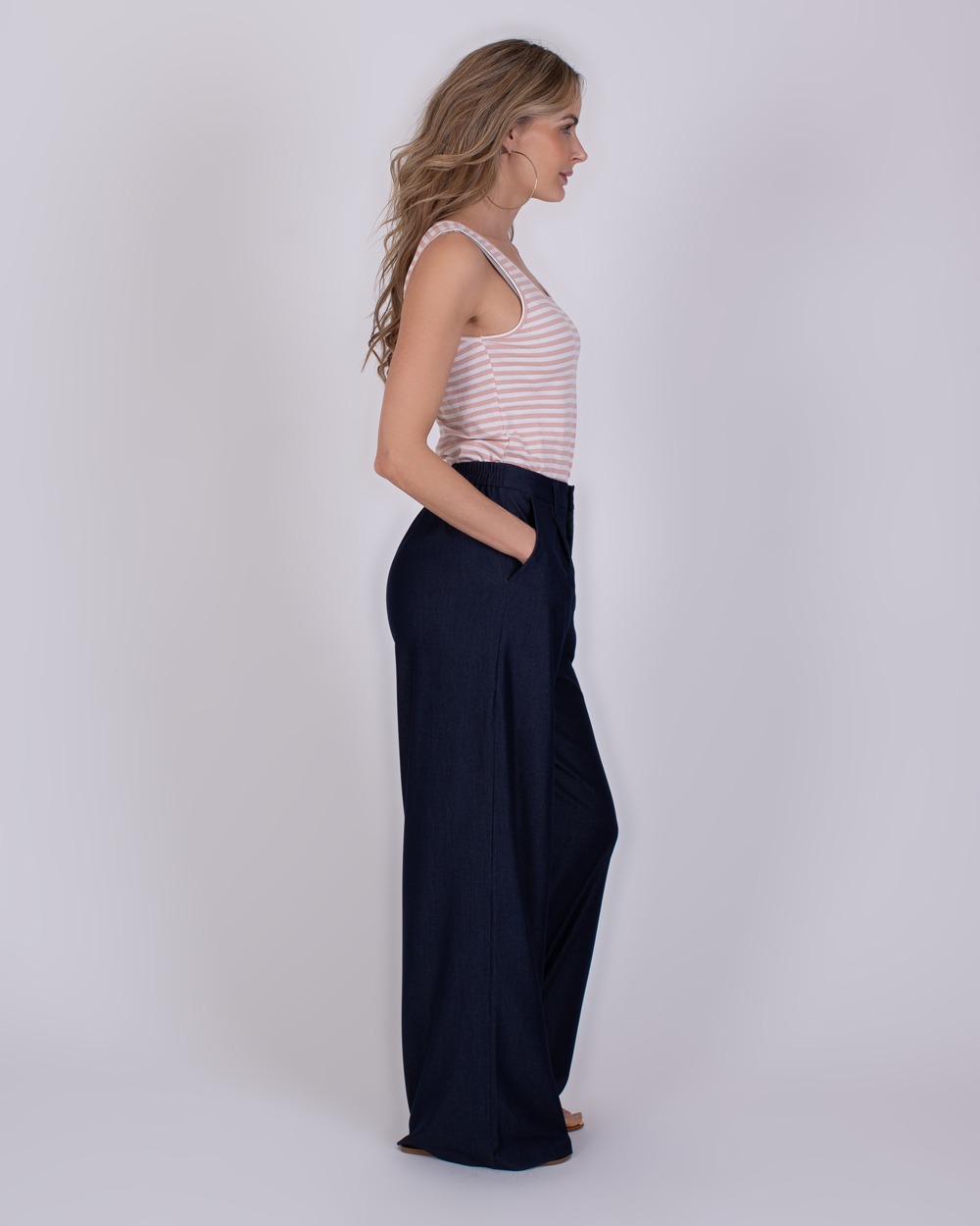 Bergamo Indigo blue 5 Vrouw in zijaanzicht draagt een Bergamo Indigo Blue 5 broek met wijde pijpen en een gestreept mouwloos topje.