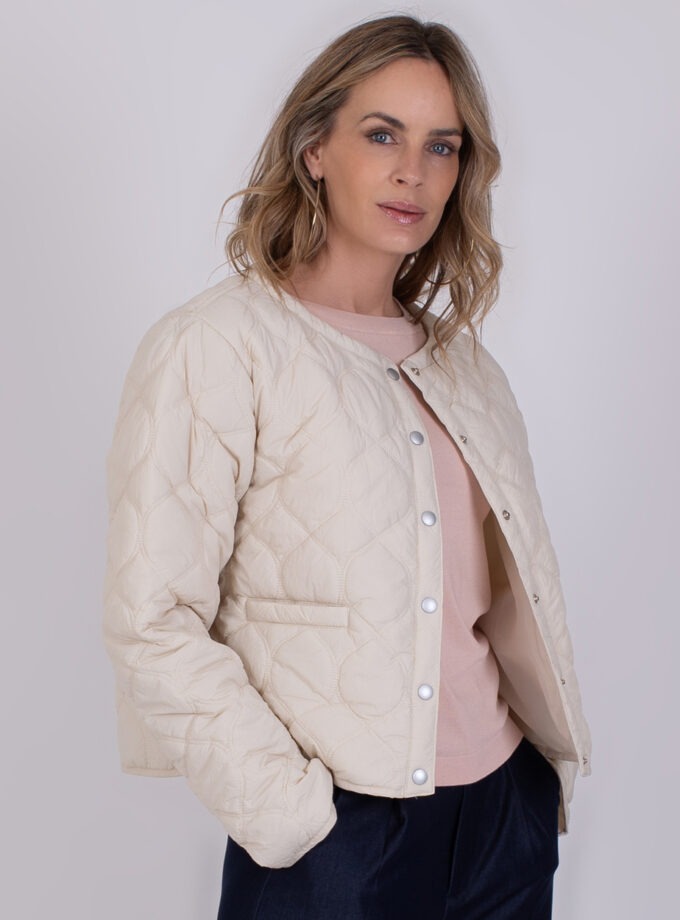 Vrouw draagt een offwhite gewatteerd jack genaamd "Burgas" met drukknoopsluiting.
