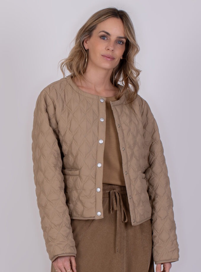 Vrouw draagt een taupekleurige, gewatteerde Burgas-jas met drukknoopsluiting.