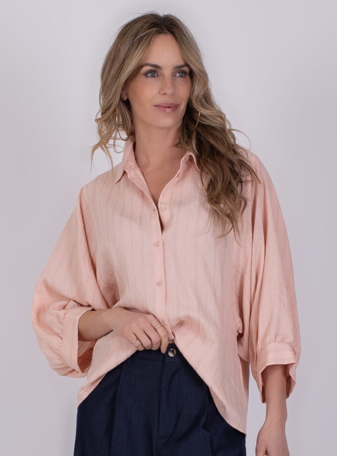 Vrouw draagt een losse, oudroze Busan-blouse met wijde mouwen en een donkerblauwe broek.