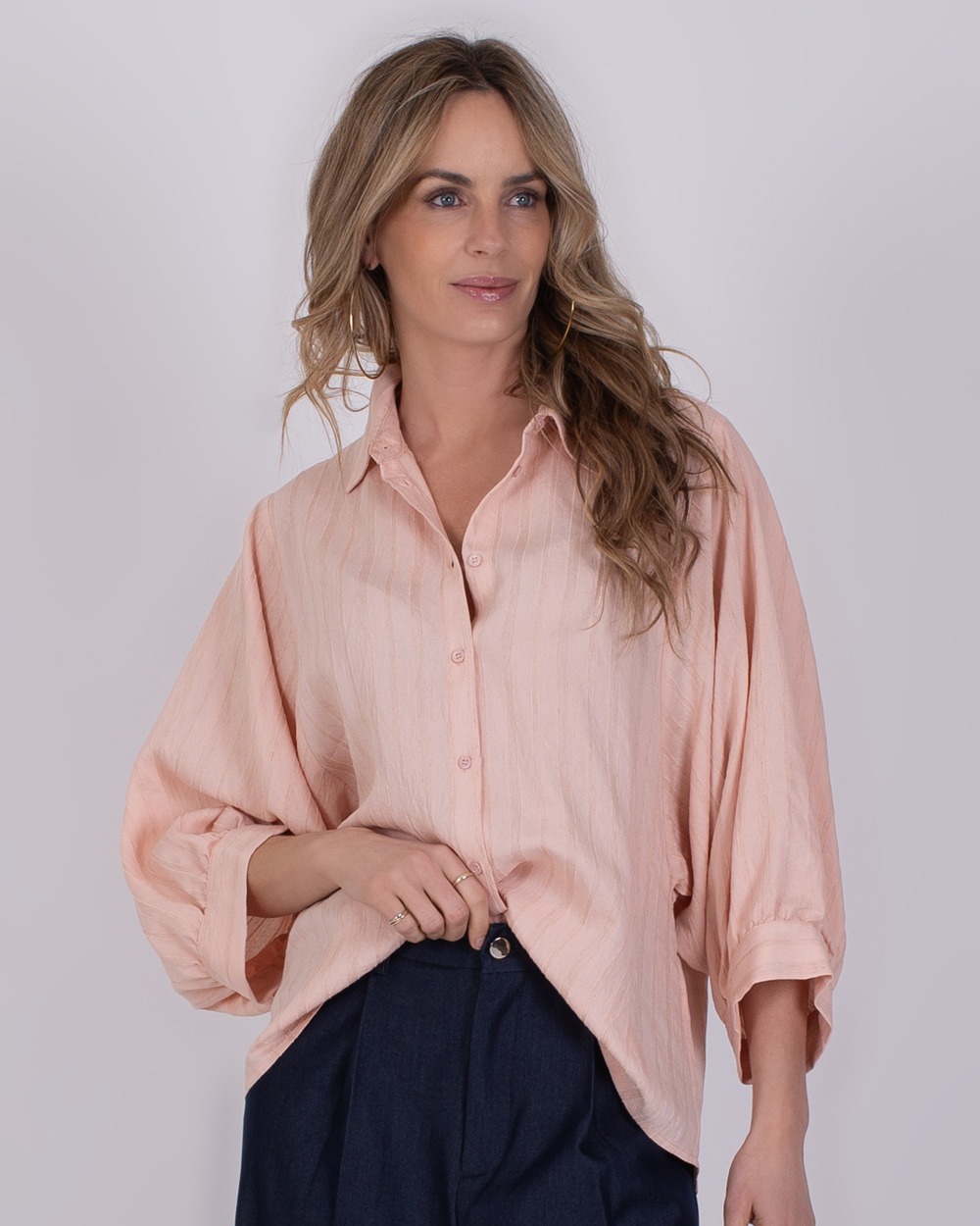 Vrouw draagt een losse, oudroze Busan-blouse met wijde mouwen en een donkerblauwe broek.