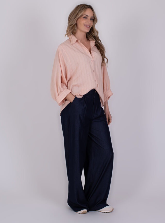 Vrouw draagt een lichtroze Busan old pink blouse met donkerblauwe, wijde broek en witte sneakers.