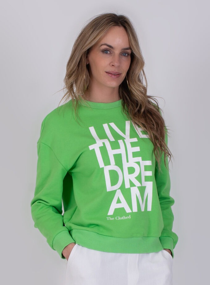 Vrouw draagt een groene Capri sweater met witte tekst "LIVE THE DREAM" op de voorkant.