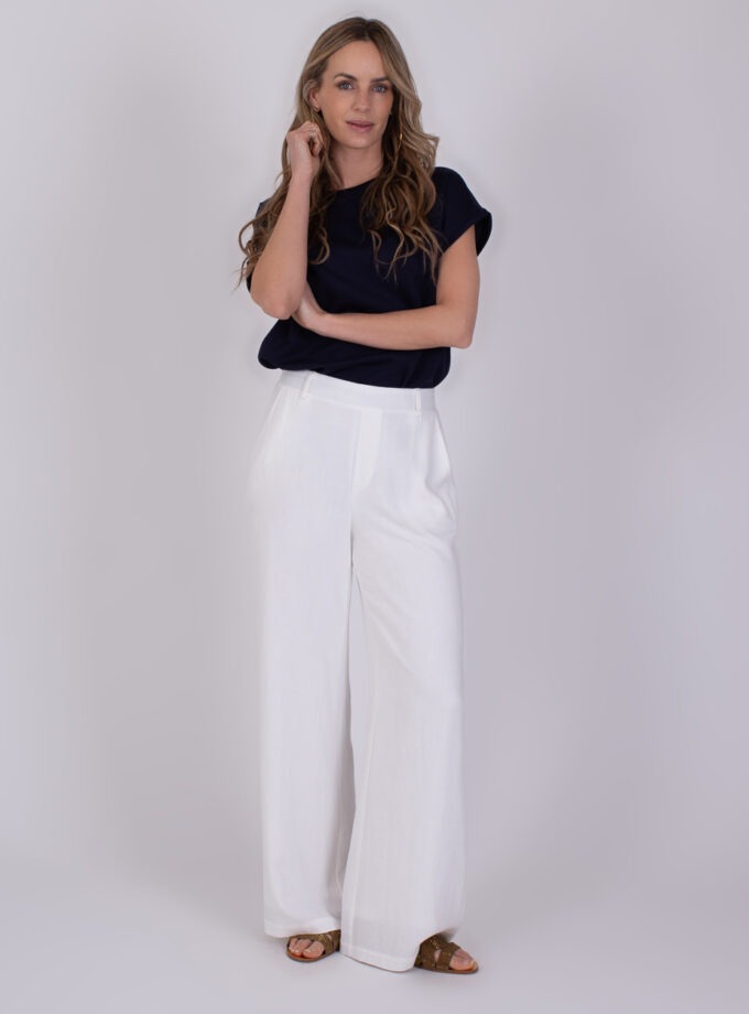 Vrouw draagt een donkerblauwe top en off-white Cebu broek met wijde pijpen.