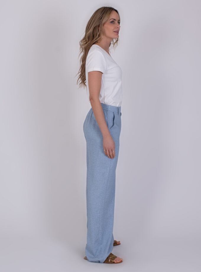 Vrouw in zijaanzicht draagt een witte T-shirt en lichtblauwe Cebu soft blue broek.